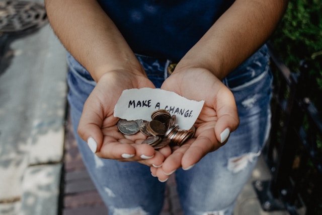 Person holding change in their hands along with a small sign that reads Make a Change